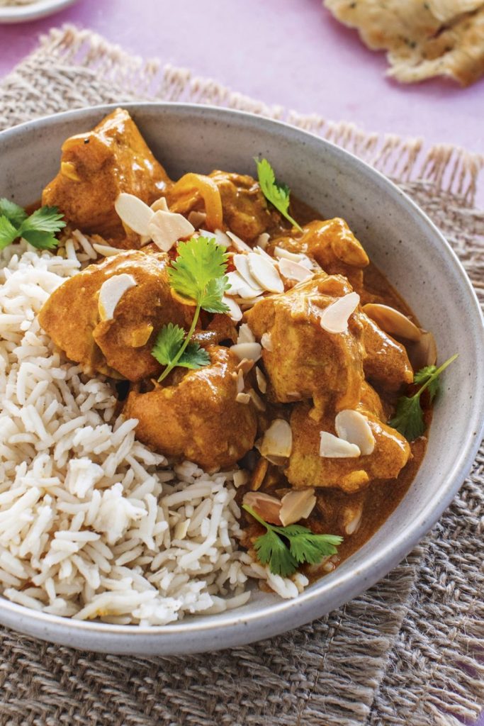 a bowl of Healthy Chicken Korma from a slow cooker, next to rice and garnished with almonds.