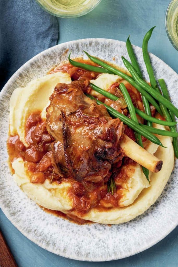 Tender lamb shanks cooked in a slow cooker, served with mashed potatoes and green beans, seasoned with rosemary.