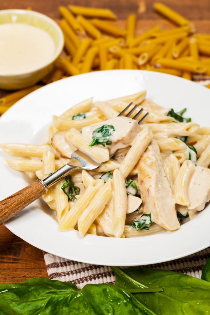 Plate of creamy chicken pasta with spinach, cooked in a slow cooker.