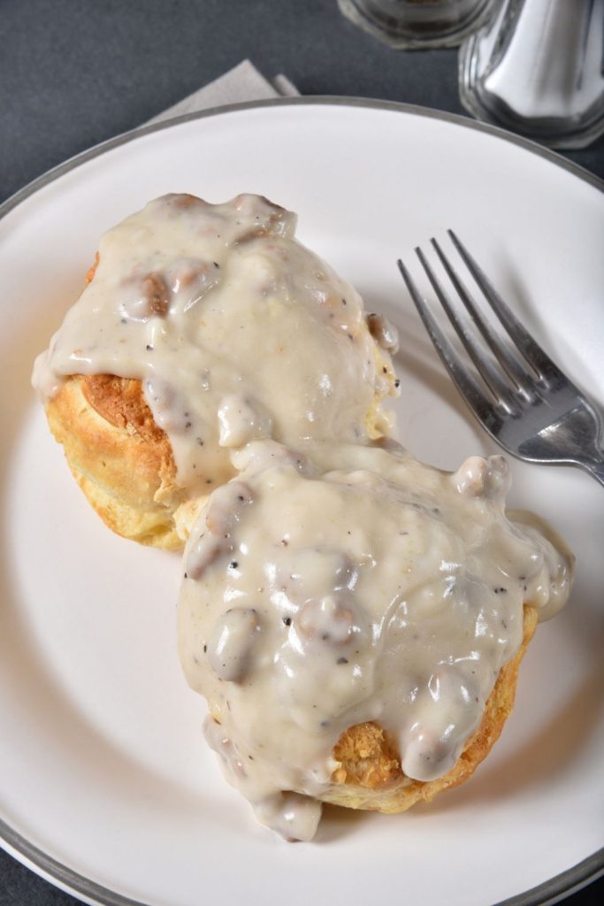 Sausage gravy on biscuits on a white plate with a fork.