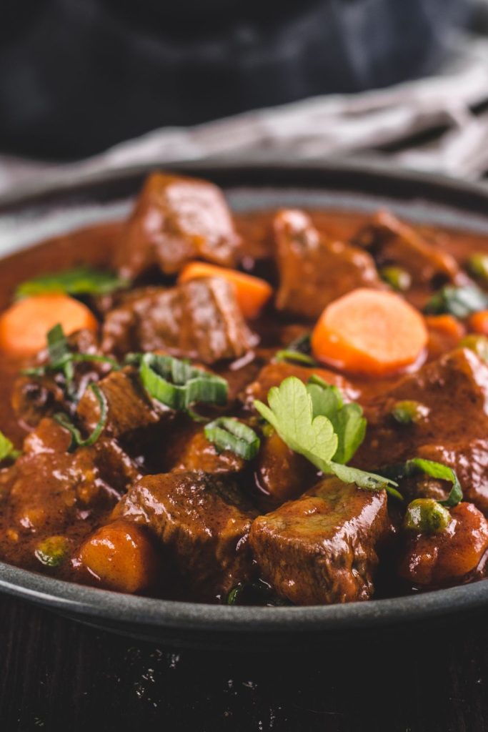 A bowl of rich and hearty slow cooker beef stew with carrots and spring onions, garnished with fresh herbs.