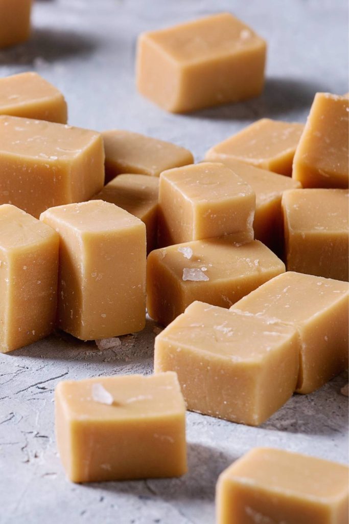Caramel fudge cubes with sugar and syrup in wooden bowls.