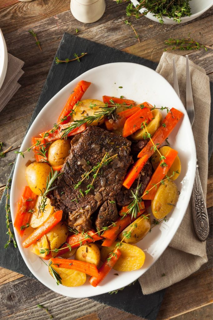Juicy slow cooker ribeye steak with roasted carrots and potatoes on a white plate.