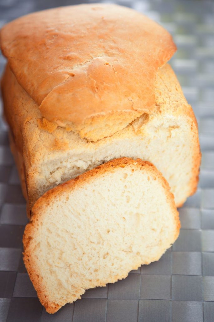A full loaf of white bread with two end slices on a cooling rack.