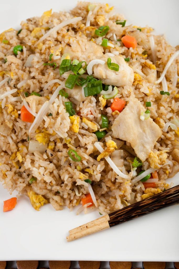 chicken fried rice with egg and vegetables on a plate with chopsticks.