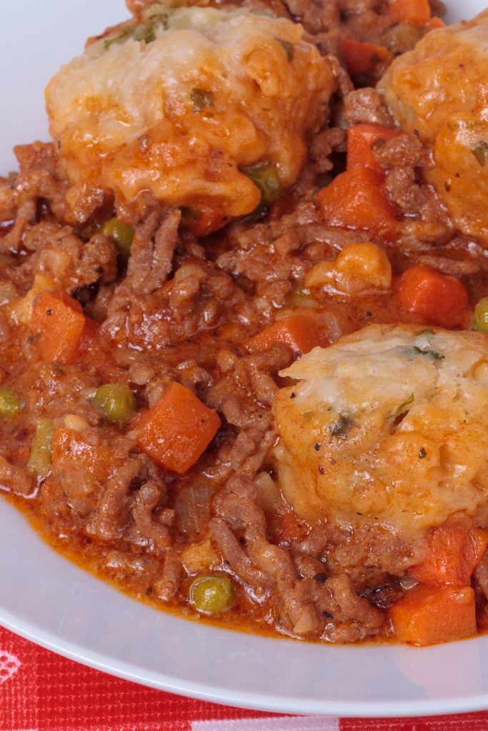 Mince with carrots and peas, and dumplings on a white plate.