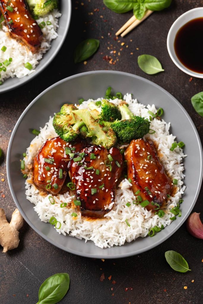 Pork belly slices with white rice and broccoli on a dish.