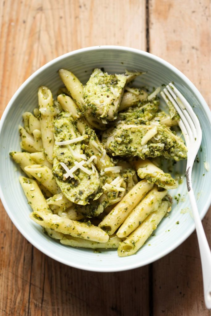 Bowl of chicken pesto pasta on a rustic wooden table.