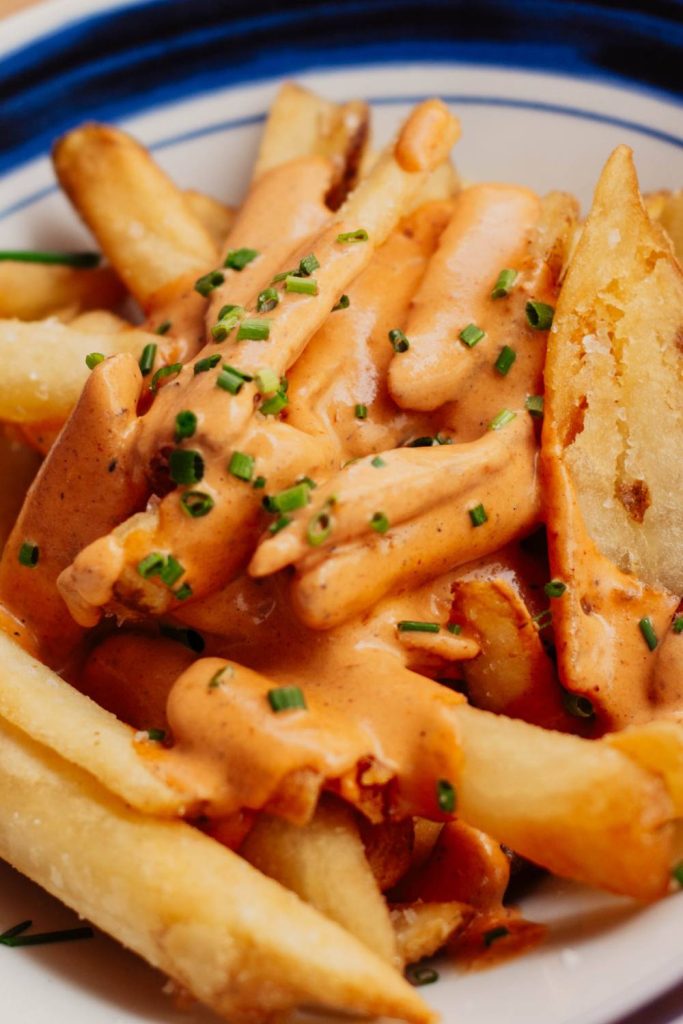 Thick-cut fries with orange sauce and chopped green onions on a plate.