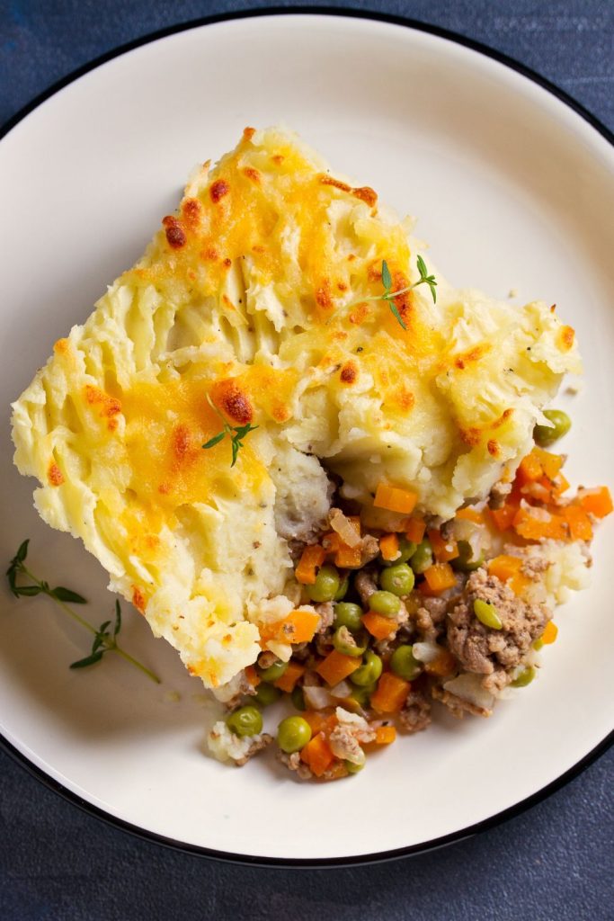 A plate of meat and potato pie with vegetables, a golden potato topping visible.
