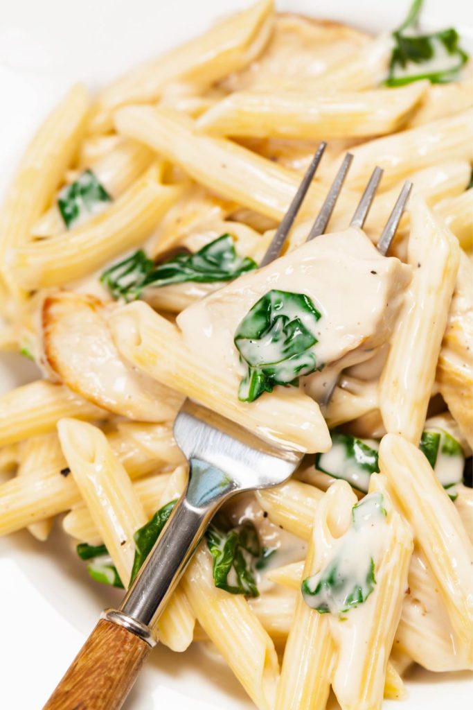 Forkful of creamy chicken pasta with spinach from a slow cooker.