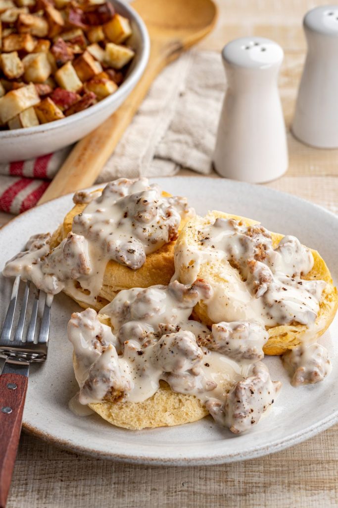 Biscuits topped with sausage gravy, next to roasted potatoes.