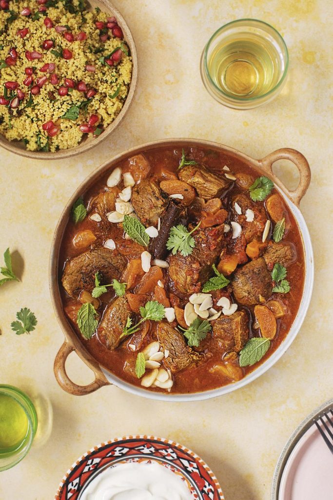 Slow Cooker Spiced Apricot Lamb Tagine garnished with almonds and herbs in a clay pot.