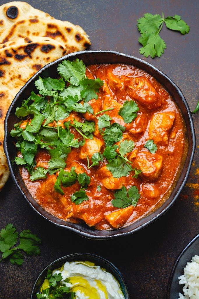 Slow Cooker Tandoori Chicken topped with cilantro in a bowl with naan and yogurt on the side.