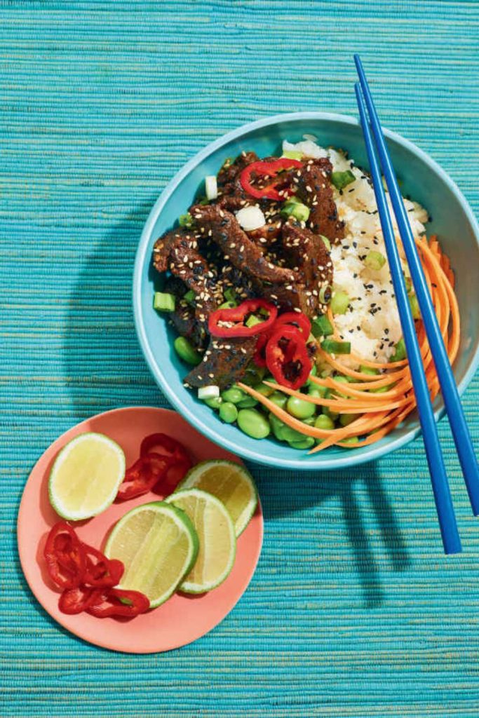 Slow cooker teriyaki beef served in a bowl with vegetables, rice, and a side of lime and chili.