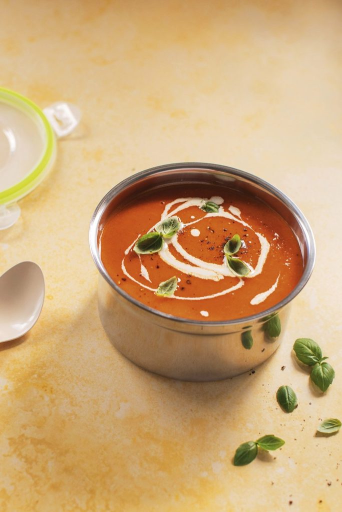 Creamy sweet potato and red pepper soup in a stainless steel bowl with a cream swirl and fresh basil.