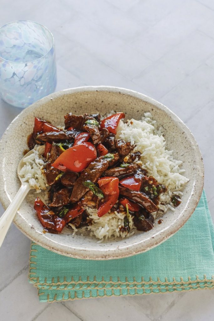 Thai Basil Beef over rice in a ceramic bowl with a glass of water.