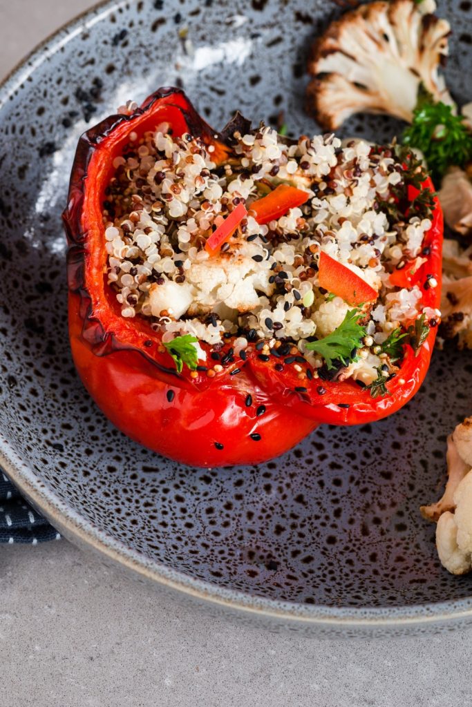 A single stuffed red capsicum filled with quinoa and vegetables on a plate.