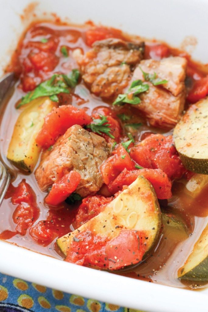 Mediterranean beef stew with tomatoes and zucchini in a white bowl.