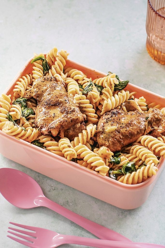 Slow Cooker Creamy Paprika Chicken Thighs with rotini pasta and spinach in a pink container.