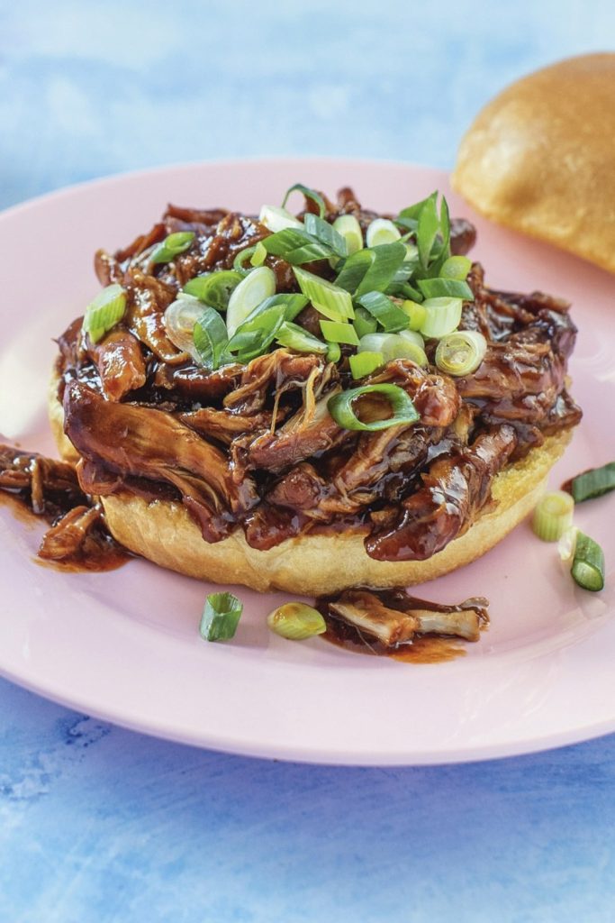 Slow Cooker Honey Garlic Shredded Chicken sandwich with green onions on a pink plate.