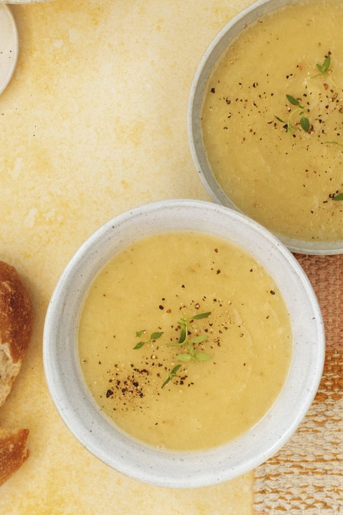 Slow Cooker Leek and Potato Soup in two bowls with pepper and bread on the side.