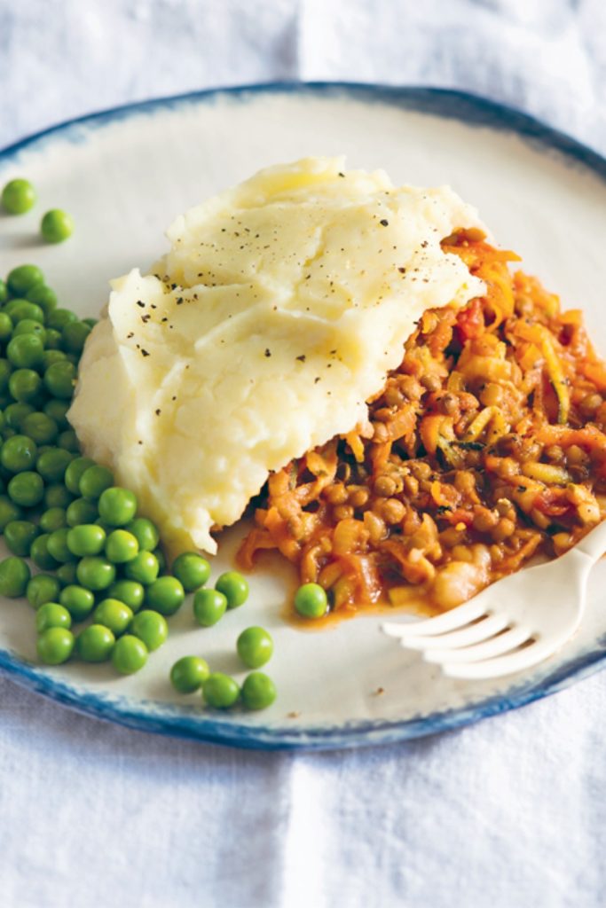 Slow Cooker Lentil Cottage Pie with mashed potatoes and green peas on a plate, fork on the side.