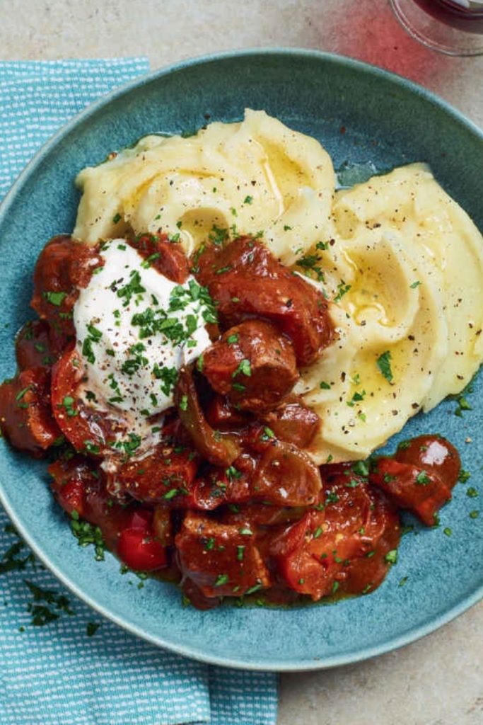 Slow Cooker Smoky Beef Goulash with Chorizo and mashed potatoes on a blue plate.