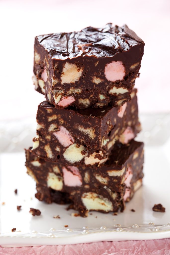 Stack of Slow Cooker Tim Tam Rocky Road pieces with marshmallows and biscuits on a white plate.