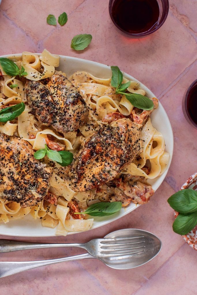 Slow Cooker Tuscan Chicken with pasta and fresh basil on a white plate.