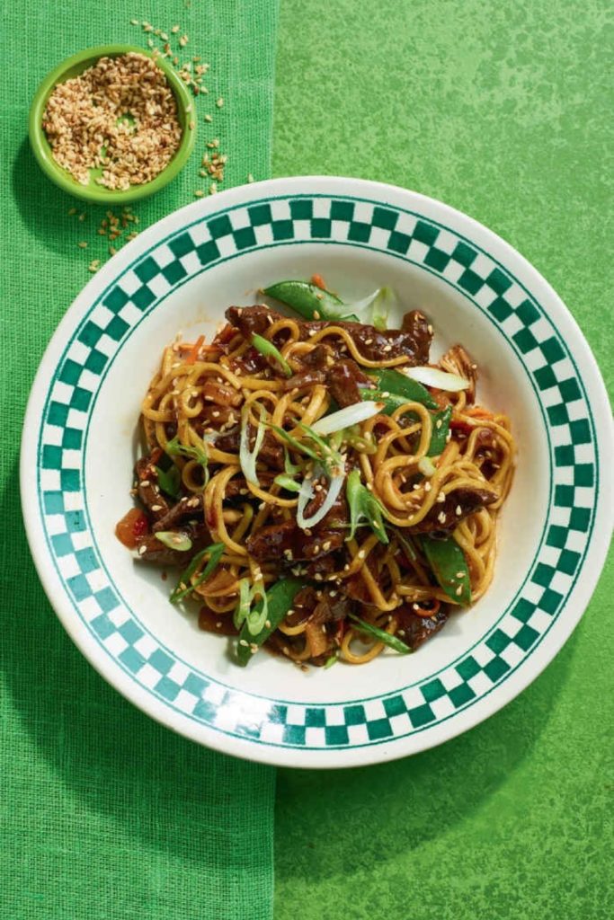 Slow Cooker Beef Chow Mein with snow peas and sesame seeds on a green background.