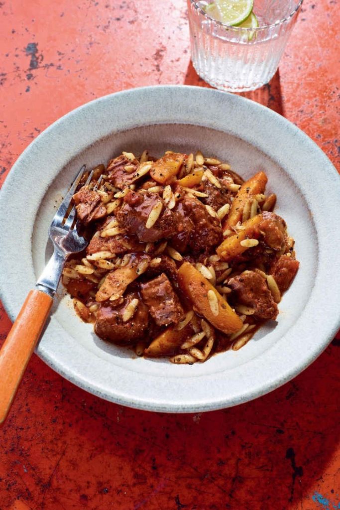 Slow Cooker Beef Stifado with orzo and slivered almonds in a ceramic bowl.