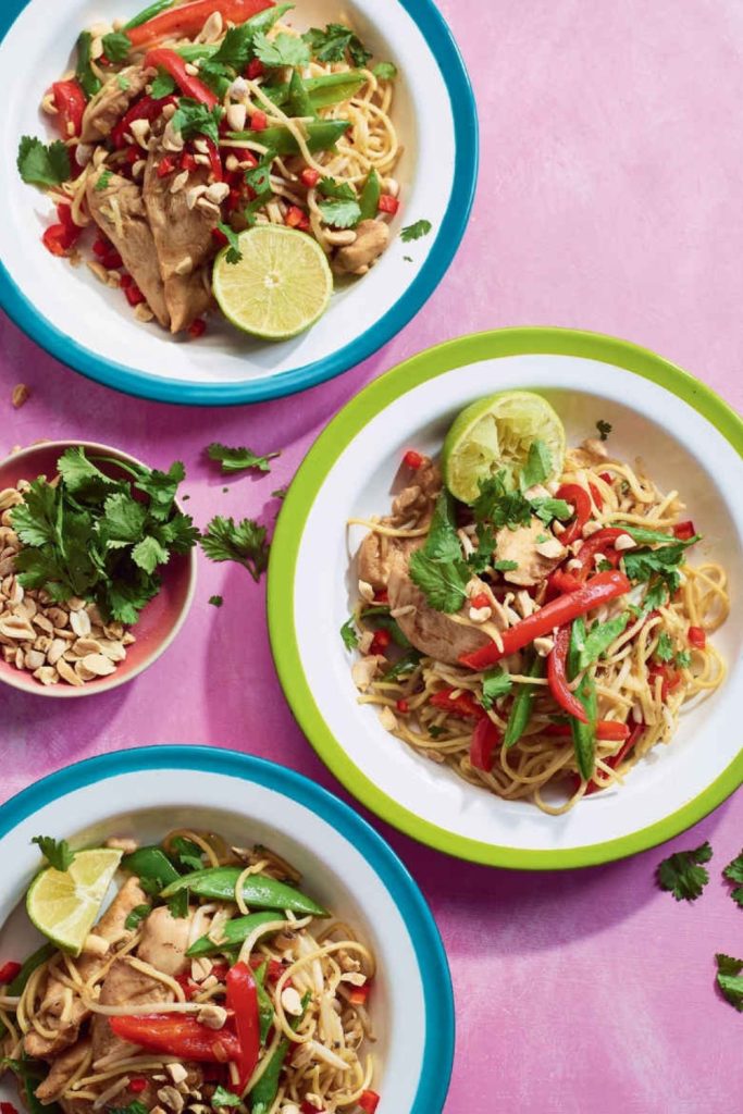 Slow Cooker Chicken Pad Thai with noodles, red bell peppers, snap peas, cilantro, and lime in colorful bowls.