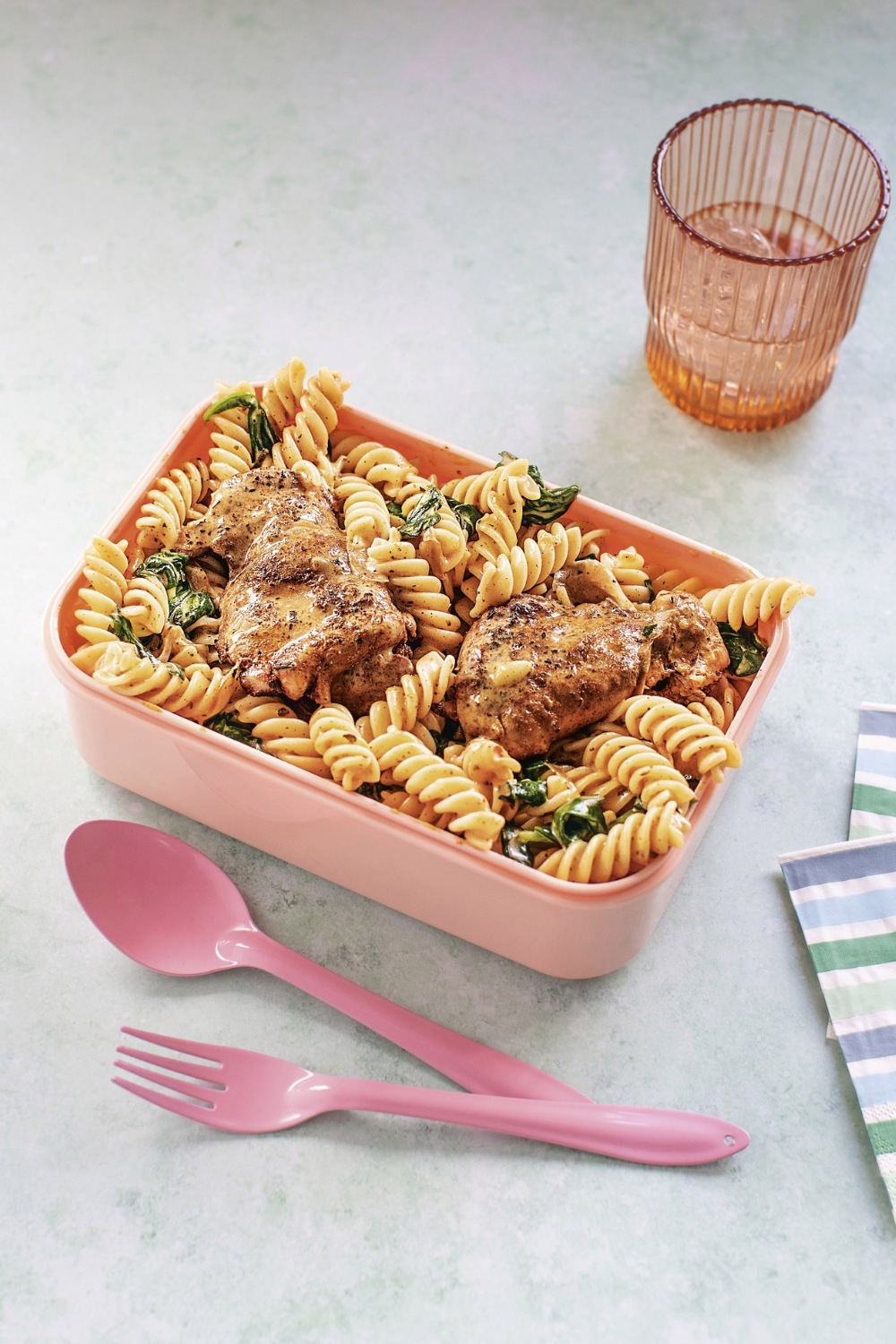 Slow Cooker Creamy Paprika Chicken Thighs with rotini pasta and spinach in a pink container.