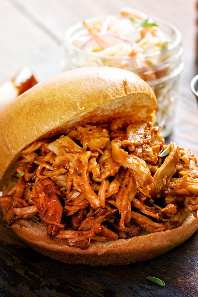 Slow Cooker Gravy Pulled Chicken in a bun with coleslaw in the background.