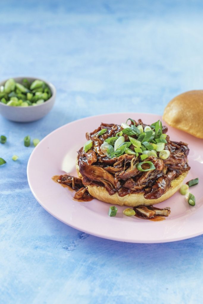Slow Cooker Honey Garlic Shredded Chicken sandwich topped with green onions on a pink plate.
