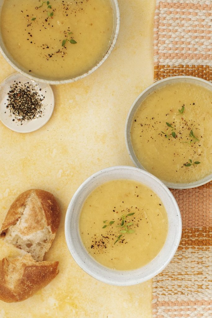 Slow Cooker Leek and Potato Soup in three bowls with pepper and bread on the side.