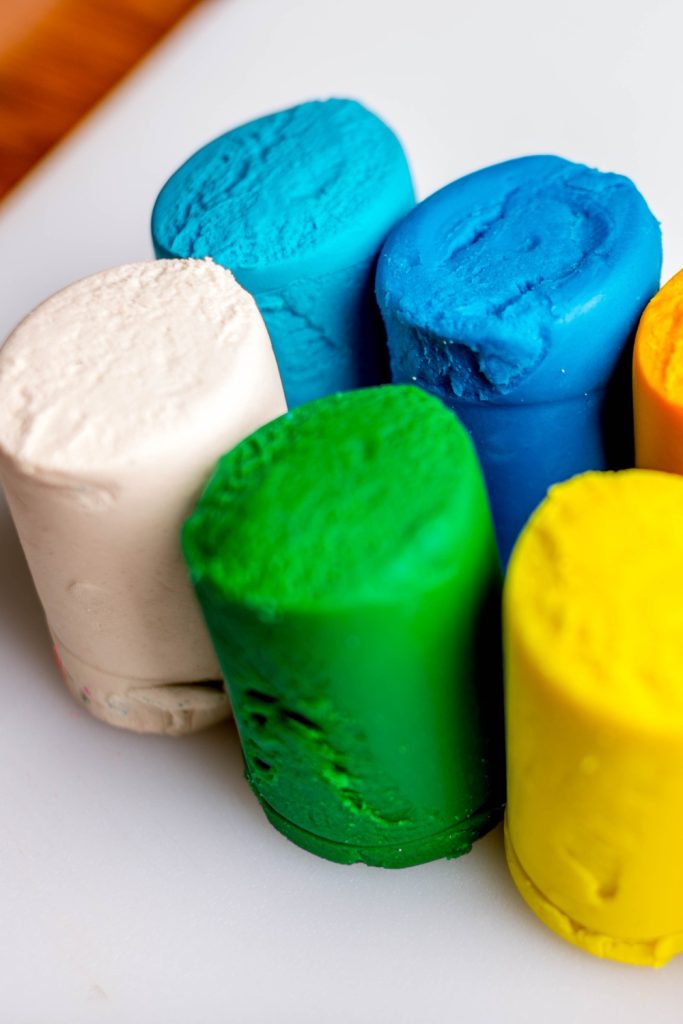 Brightly colored homemade playdough cylinders on a white surface.