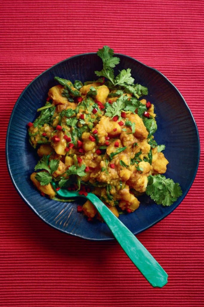 Slow Cooker Saag Aloo with vibrant spices, served in a blue dish on a red background.