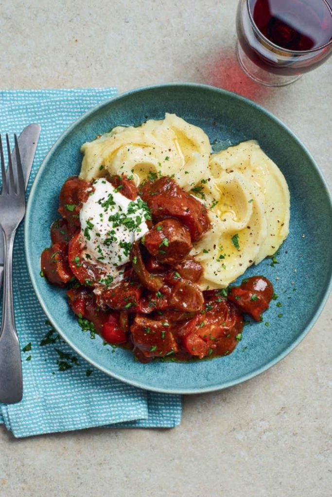 Slow Cooker Smoky Beef Goulash with Chorizo, served with mashed potatoes on a blue plate.