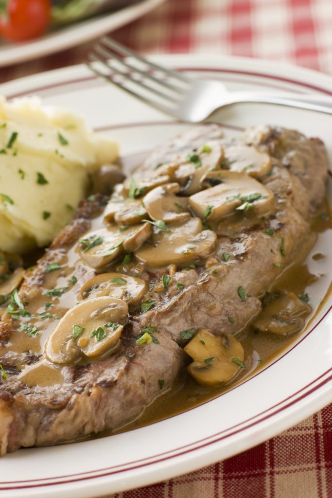 Slow Cooker Steak Diane with mushrooms and sauce, served with mashed potatoes.