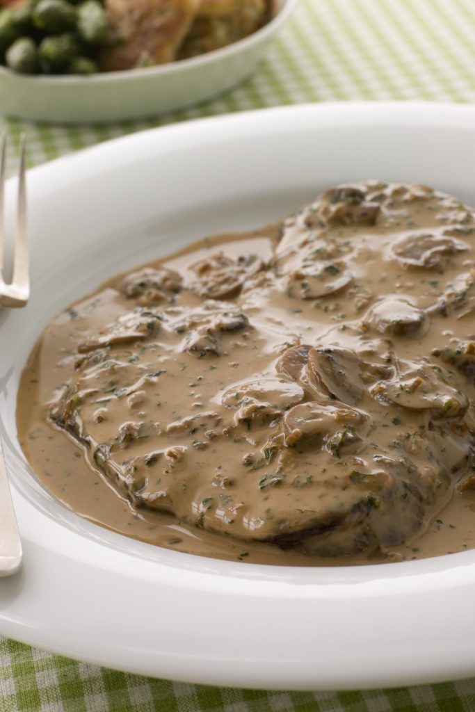 Slow Cooker Steak Diane covered in a rich mushroom sauce on a white plate.