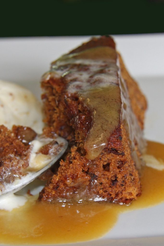 Slow Cooker Sticky Date Pudding with caramel sauce, honeycomb, and a cup of sauce on a plate.