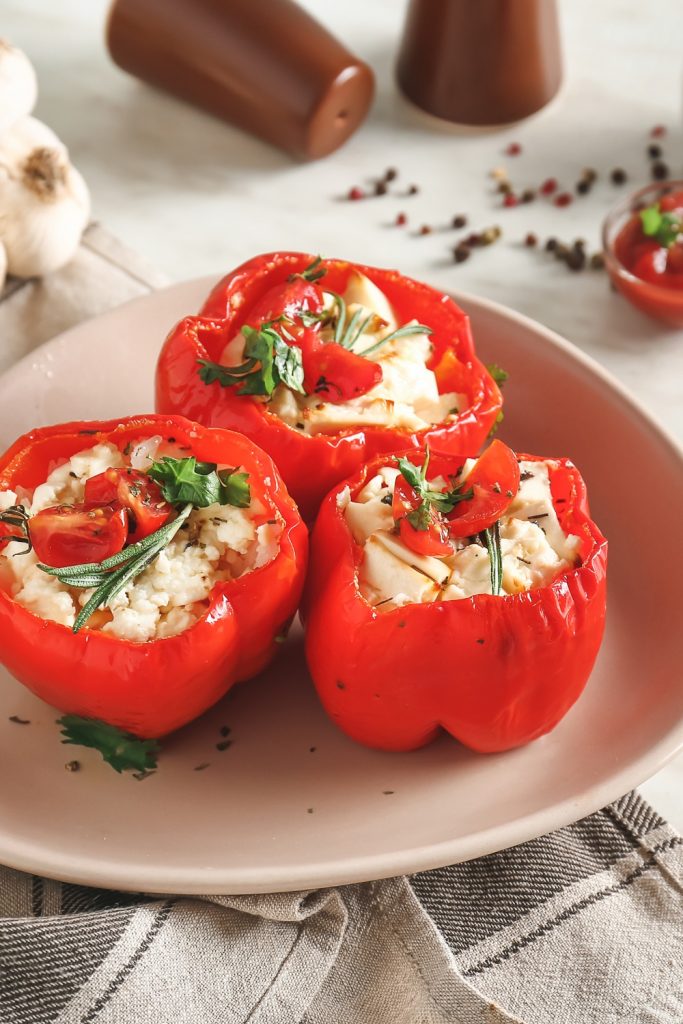 Three stuffed red capsicums filled with rice and vegetables on a plate.