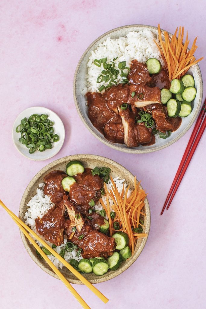 Slow Cooker Sweet and Spicy Pork served with rice, cucumber slices, shredded carrots, and green onions in two bowls.