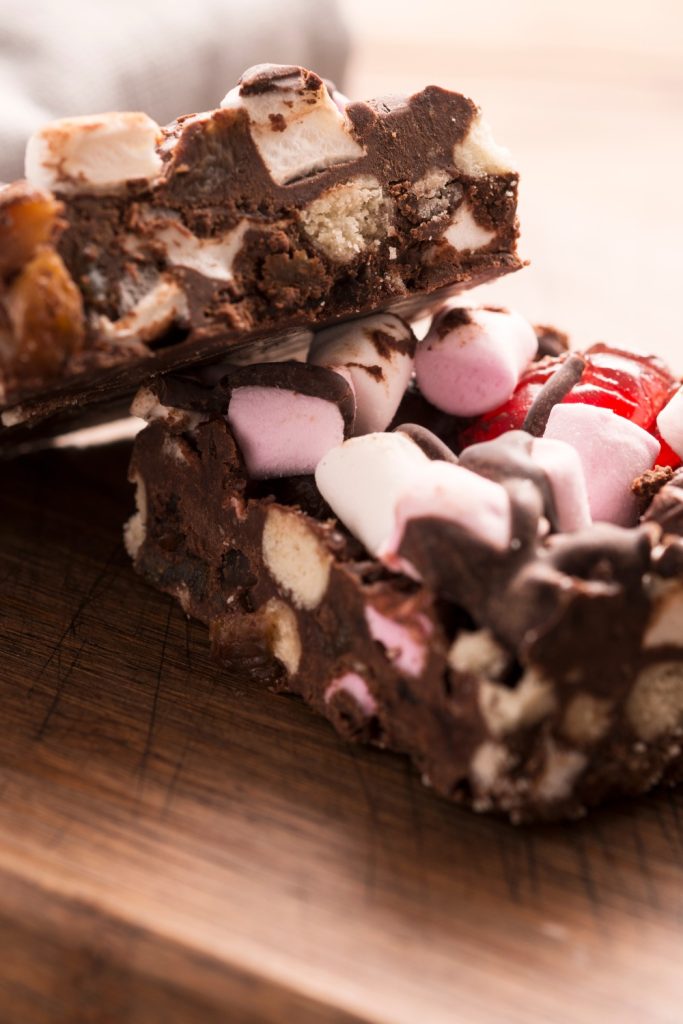Slices of Slow Cooker Tim Tam Rocky Road with marshmallows and biscuits on a wooden board.