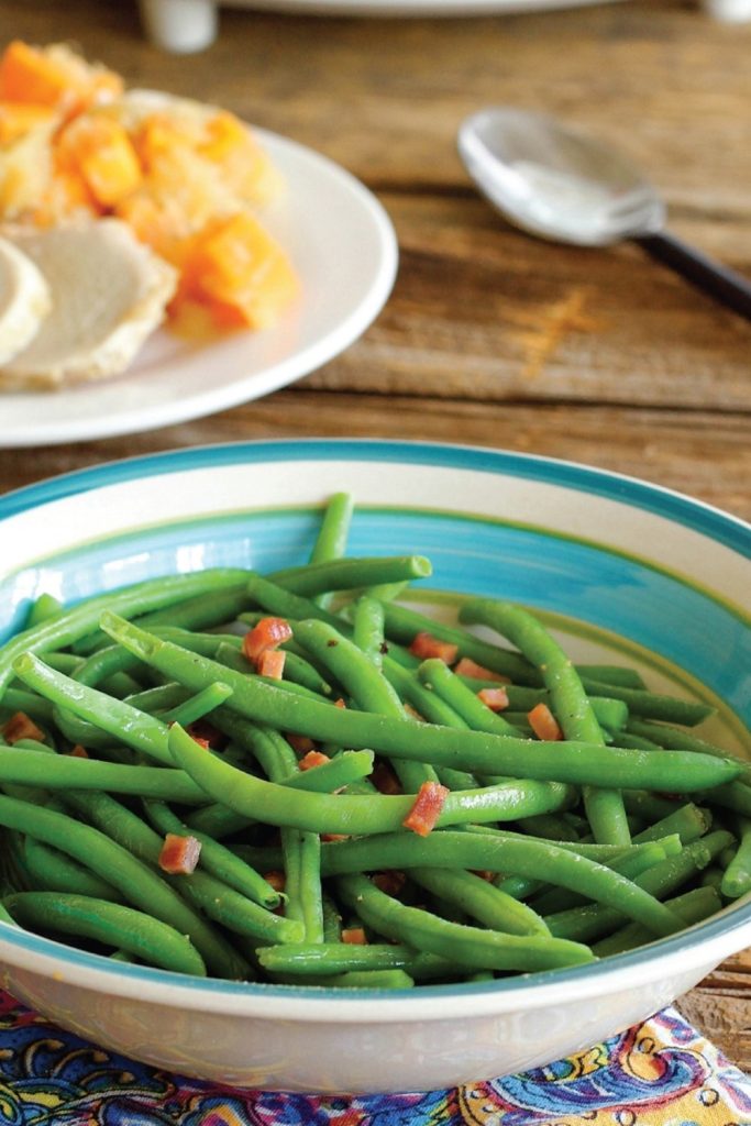 Fresh green beans with bacon bits in a blue-rimmed white bowl.