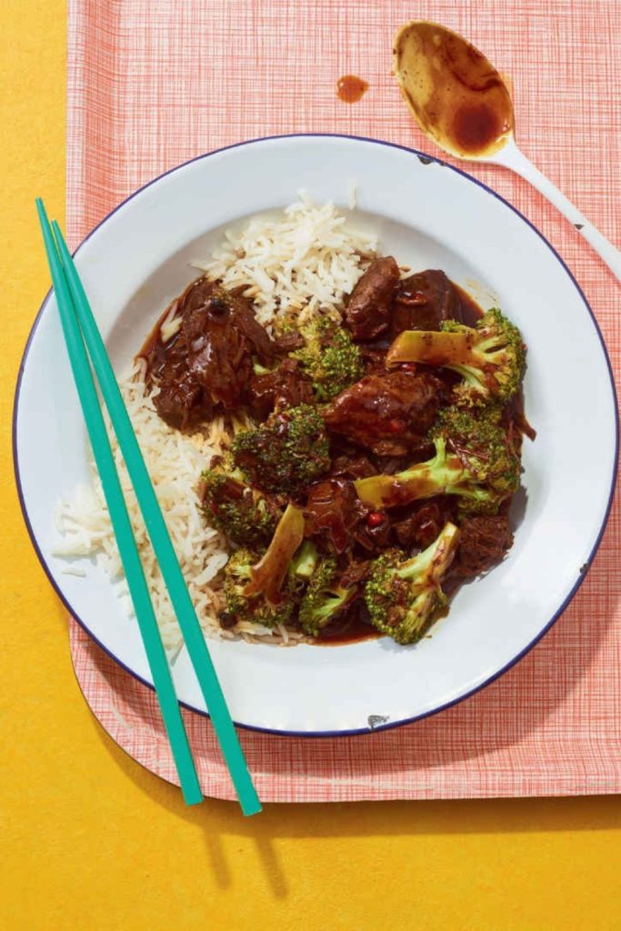 Slow cooker beef adobo with broccoli on white rice, served with green chopsticks.