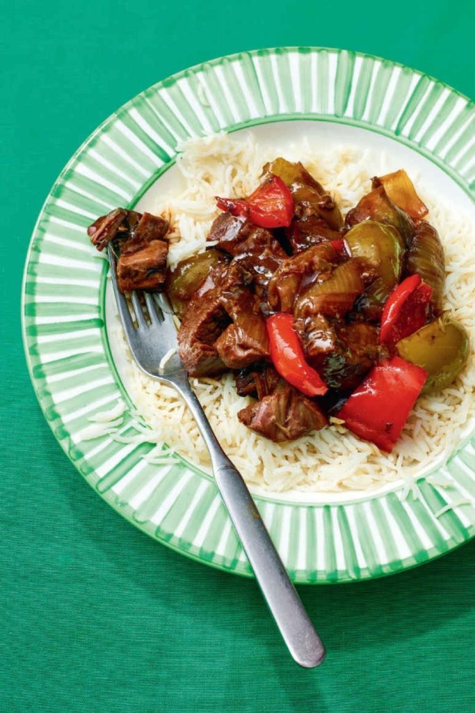 Slow cooker black pepper beef with bell peppers on white rice in a green-striped plate.
