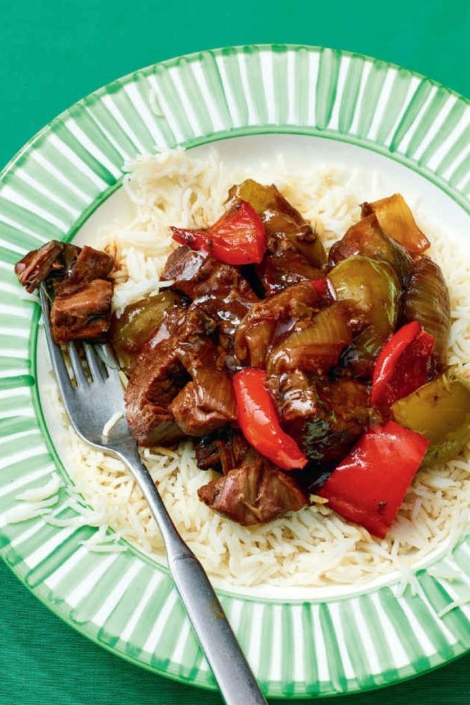 slow cooker black pepper beef with bell peppers on a plate of white rice.